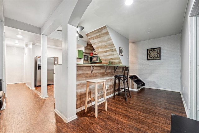 bar with wood finished floors, brick wall, baseboards, stainless steel fridge with ice dispenser, and a bar