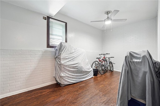 miscellaneous room featuring ceiling fan, brick wall, and wood finished floors