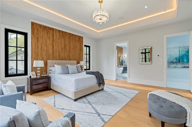 bedroom with a tray ceiling, multiple windows, and light wood-style flooring