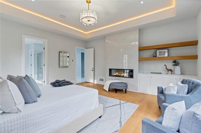 bedroom featuring visible vents, connected bathroom, a tray ceiling, a premium fireplace, and light wood-style floors