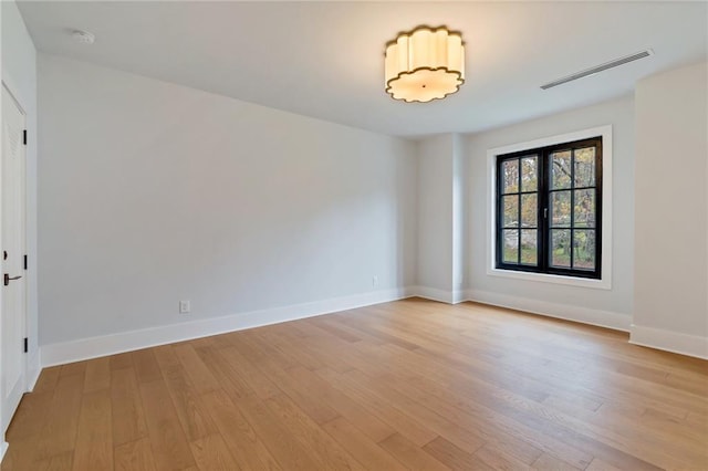 empty room with light wood finished floors, visible vents, and baseboards