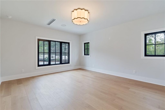 empty room featuring light wood-type flooring, visible vents, and baseboards