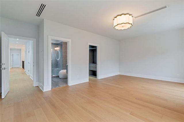 unfurnished bedroom with ensuite bath, baseboards, visible vents, and light wood-type flooring