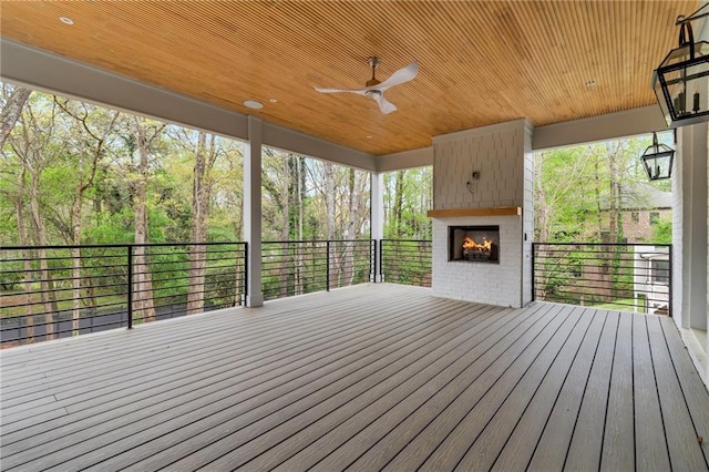 deck with an outdoor brick fireplace and ceiling fan