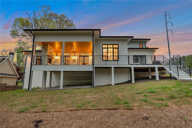 back of property at dusk with stairway, a lawn, and a wooden deck