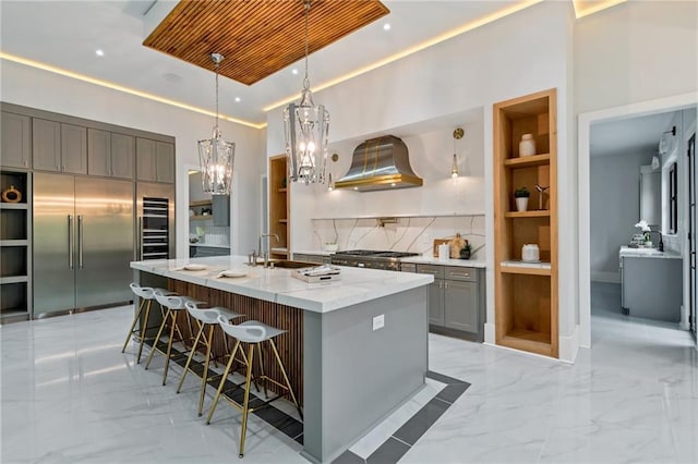 kitchen with gray cabinetry, wall chimney range hood, marble finish floor, stainless steel appliances, and a sink