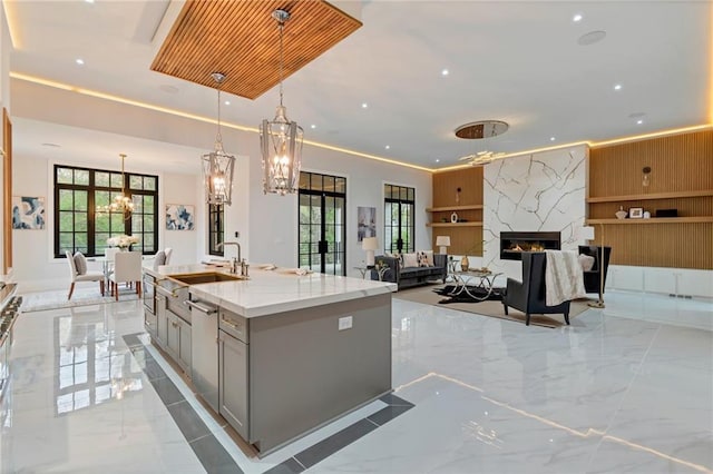 kitchen featuring marble finish floor, an island with sink, gray cabinetry, a sink, and light stone countertops