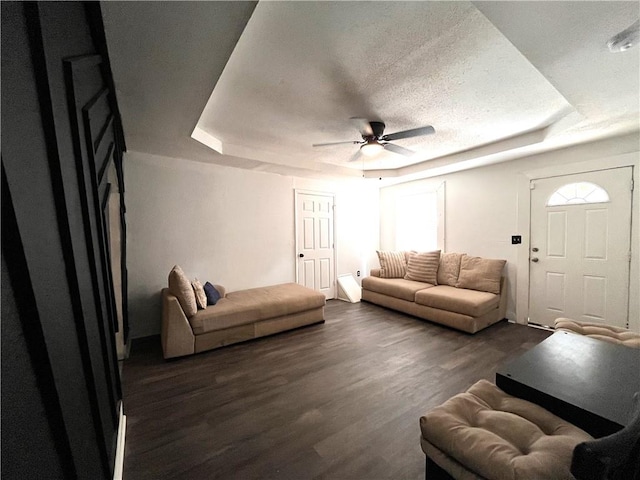 living room featuring dark hardwood / wood-style flooring, a tray ceiling, ceiling fan, and a healthy amount of sunlight