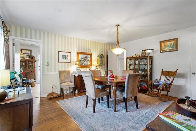 dining room with wood finished floors, baseboards, and wallpapered walls