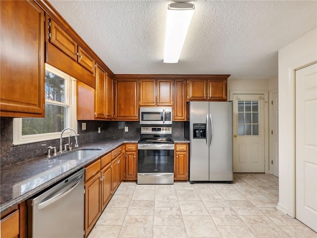 kitchen featuring sink, dark stone counters, decorative backsplash, stainless steel appliances, and a textured ceiling