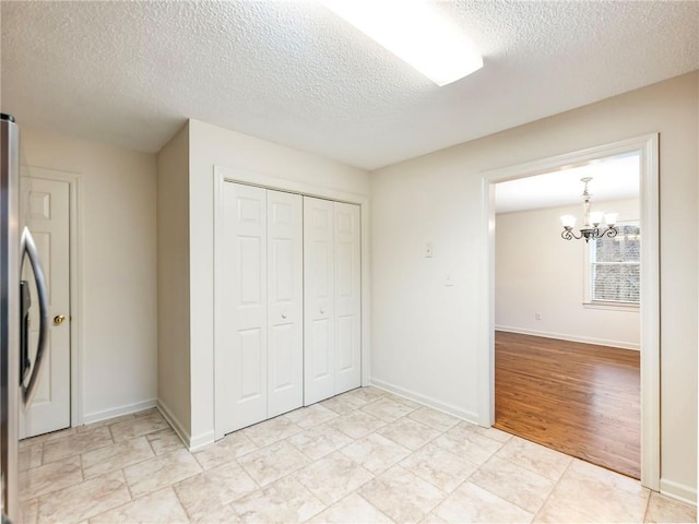 unfurnished bedroom featuring stainless steel refrigerator, an inviting chandelier, a closet, and a textured ceiling