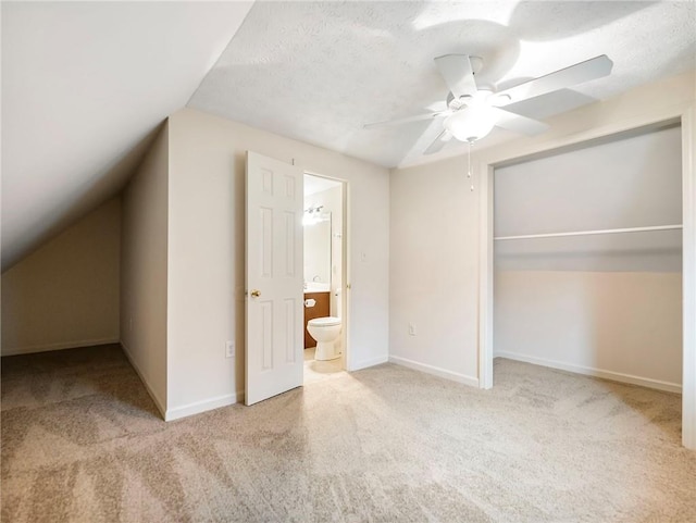 unfurnished bedroom with ceiling fan, connected bathroom, a textured ceiling, vaulted ceiling, and light colored carpet