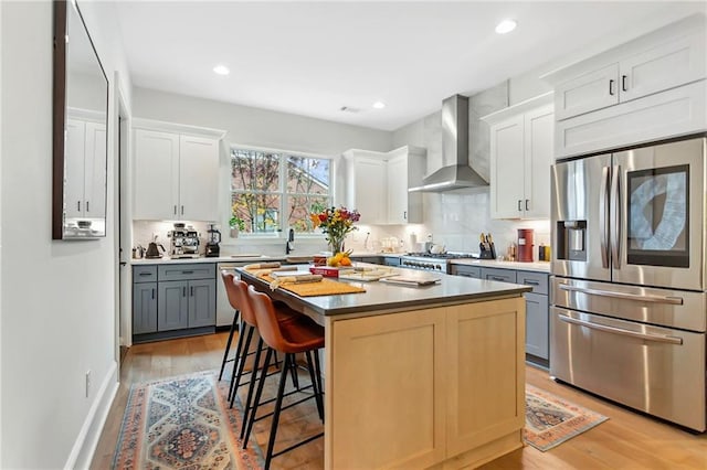 kitchen with a center island, gray cabinetry, stainless steel appliances, white cabinets, and wall chimney exhaust hood