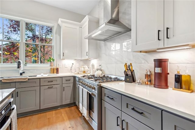 kitchen featuring wall chimney range hood, gray cabinets, white cabinetry, light hardwood / wood-style flooring, and stainless steel appliances