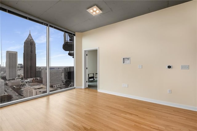 unfurnished room with baseboards, a view of city, wood finished floors, and floor to ceiling windows