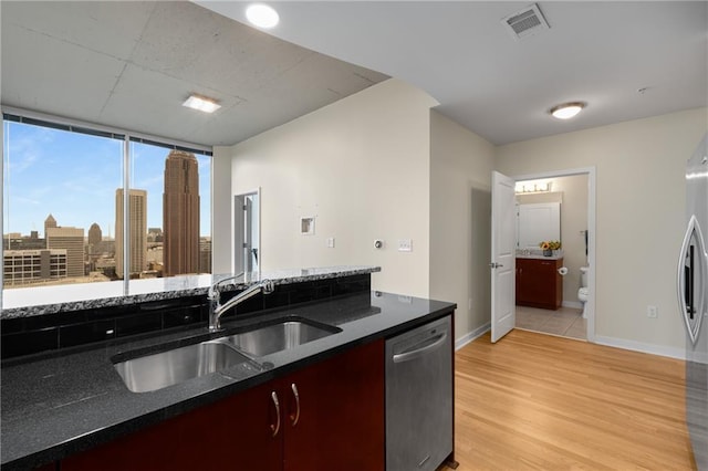 kitchen with a city view, stainless steel appliances, visible vents, a sink, and light wood-type flooring