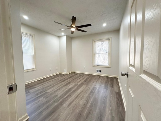 unfurnished room featuring dark wood-style flooring, visible vents, a textured ceiling, and baseboards