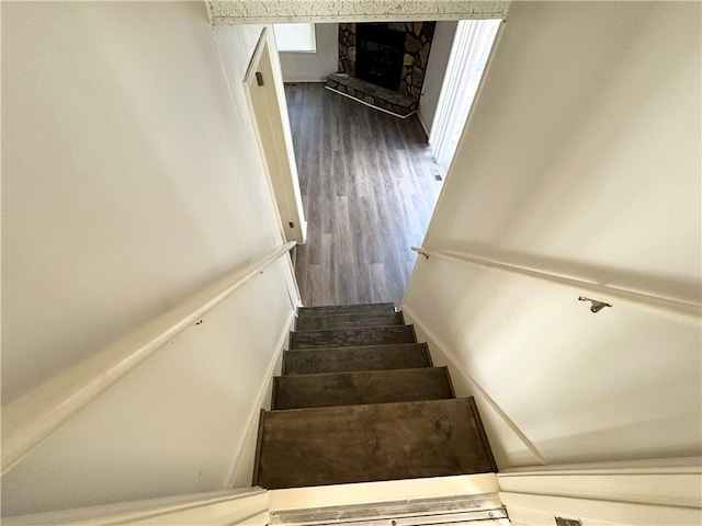 stairway featuring a stone fireplace and wood finished floors