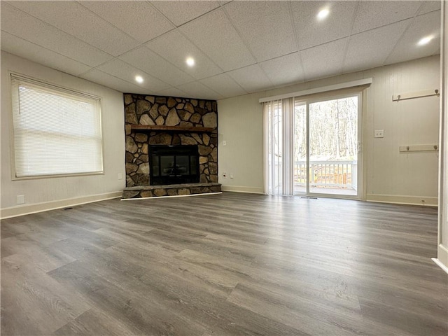 unfurnished living room with a stone fireplace, wood finished floors, a paneled ceiling, and baseboards