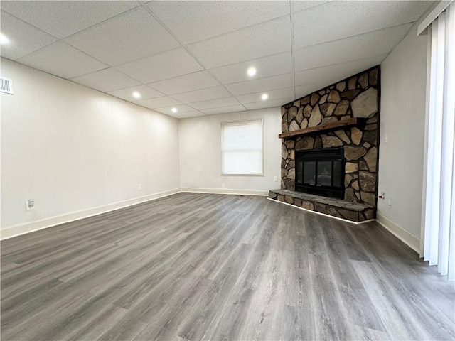 unfurnished living room featuring a fireplace, visible vents, wood finished floors, a drop ceiling, and baseboards