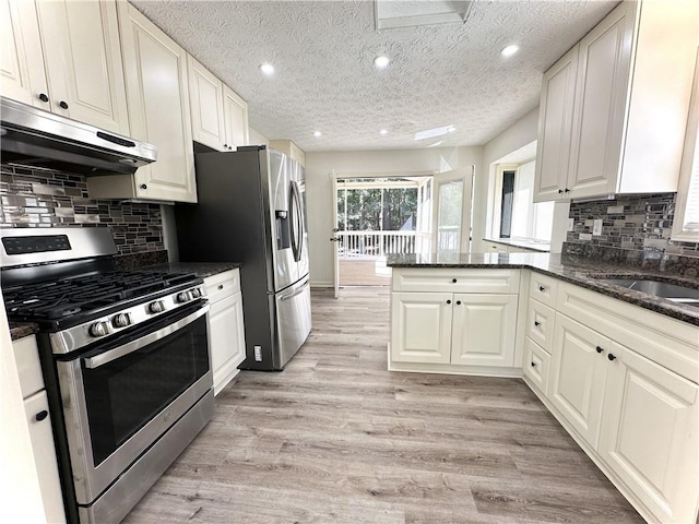 kitchen with appliances with stainless steel finishes, light wood-style floors, dark stone counters, a peninsula, and extractor fan