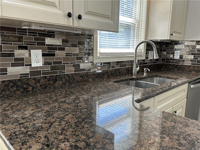 kitchen featuring tasteful backsplash, stainless steel dishwasher, white cabinetry, a sink, and dark stone counters