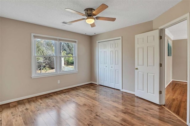 unfurnished bedroom with a textured ceiling, ceiling fan, a closet, and wood-type flooring