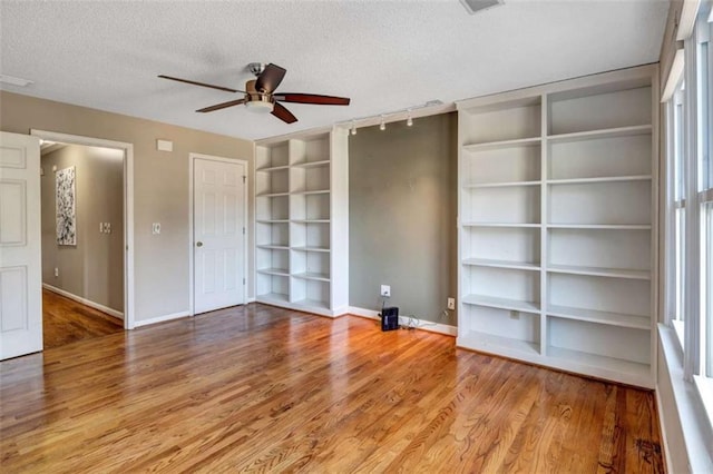 unfurnished living room featuring ceiling fan, a textured ceiling, hardwood / wood-style flooring, and built in shelves