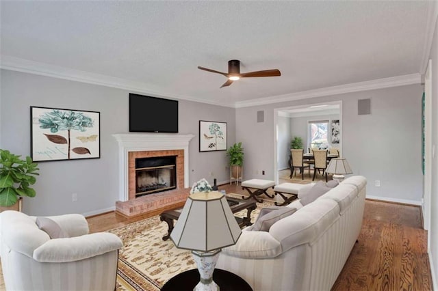 living room with a brick fireplace, wood-type flooring, ornamental molding, and ceiling fan