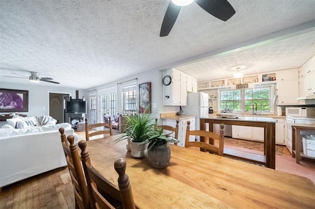 dining area featuring ceiling fan, sink, light wood-type flooring, and a textured ceiling