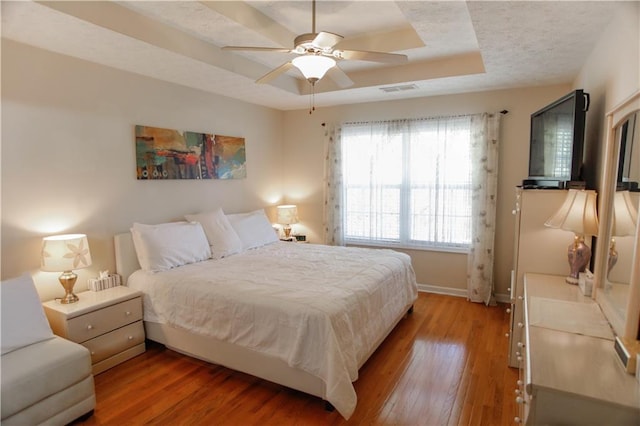 bedroom featuring ceiling fan, hardwood / wood-style flooring, a raised ceiling, and a textured ceiling