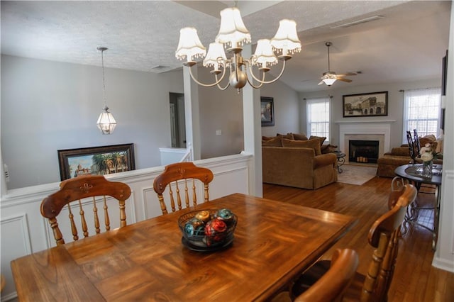 dining space featuring vaulted ceiling, ceiling fan with notable chandelier, hardwood / wood-style floors, and a textured ceiling