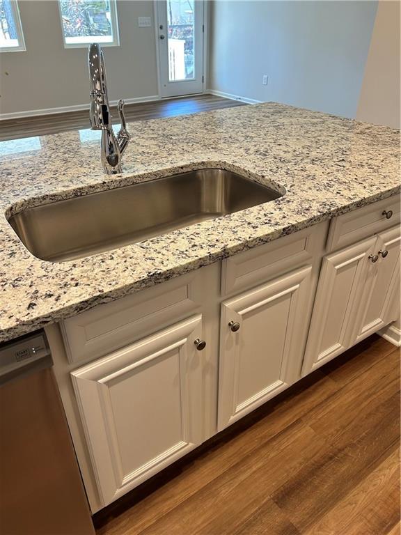 kitchen featuring white cabinetry, dishwasher, sink, dark wood-type flooring, and light stone counters