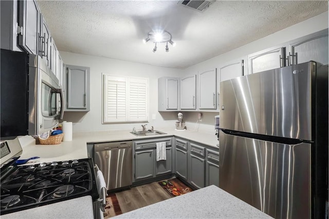 kitchen with appliances with stainless steel finishes, gray cabinetry, a textured ceiling, dark wood-type flooring, and sink