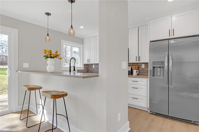 kitchen with stainless steel refrigerator with ice dispenser, a kitchen breakfast bar, tasteful backsplash, white cabinetry, and light wood finished floors