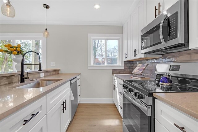 kitchen featuring tasteful backsplash, baseboards, ornamental molding, appliances with stainless steel finishes, and a sink