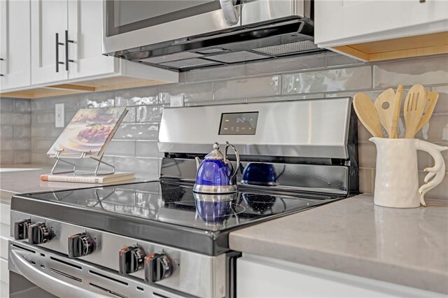 kitchen featuring decorative backsplash, white cabinets, stainless steel appliances, and light stone countertops