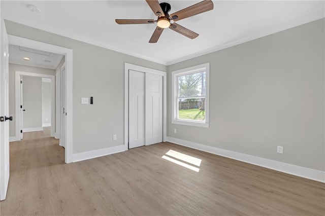 unfurnished bedroom featuring baseboards, attic access, light wood-type flooring, ornamental molding, and a closet