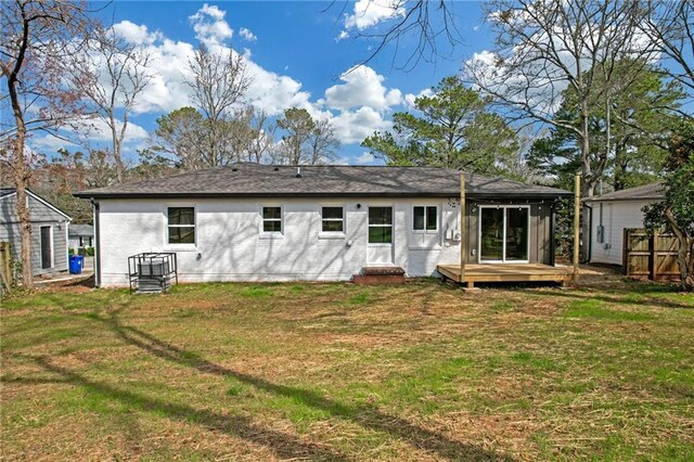 rear view of house featuring a wooden deck, a lawn, and a shingled roof