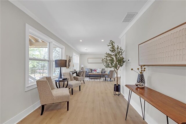 living area with visible vents, light wood-type flooring, baseboards, and ornamental molding