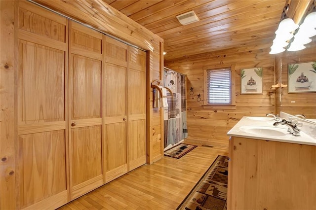 full bathroom featuring wooden walls, wood ceiling, an inviting chandelier, wood finished floors, and a sink