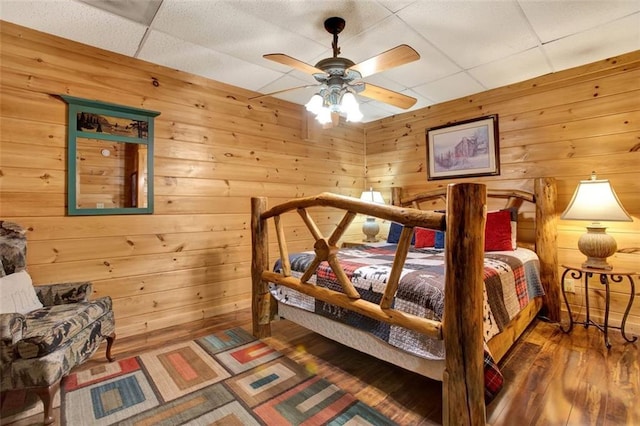 bedroom featuring wooden walls, a paneled ceiling, ceiling fan, and wood finished floors