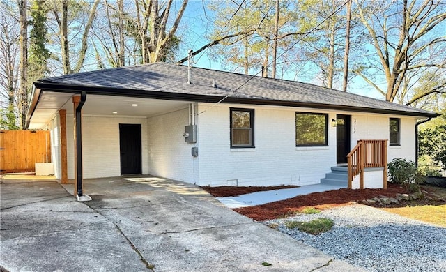 ranch-style home featuring driveway, fence, a shingled roof, an attached carport, and brick siding