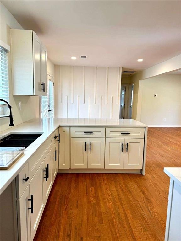 kitchen featuring light countertops, wood finished floors, a peninsula, and a sink