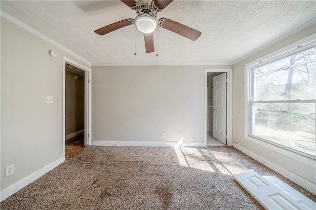 carpeted empty room with a ceiling fan, a textured ceiling, baseboards, and crown molding