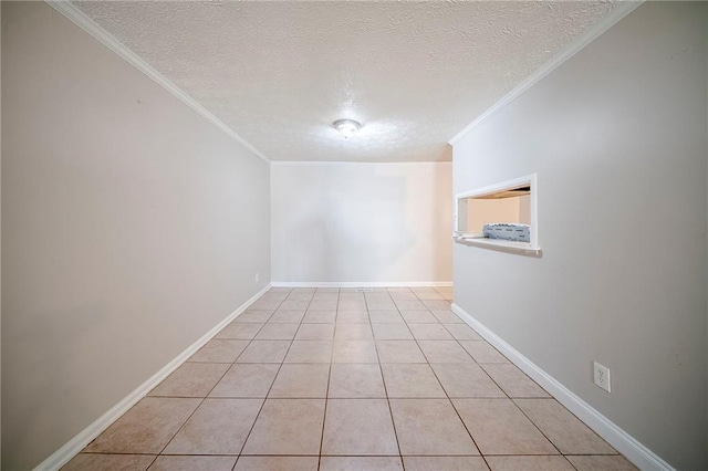 empty room with light tile patterned floors, ornamental molding, a textured ceiling, and baseboards