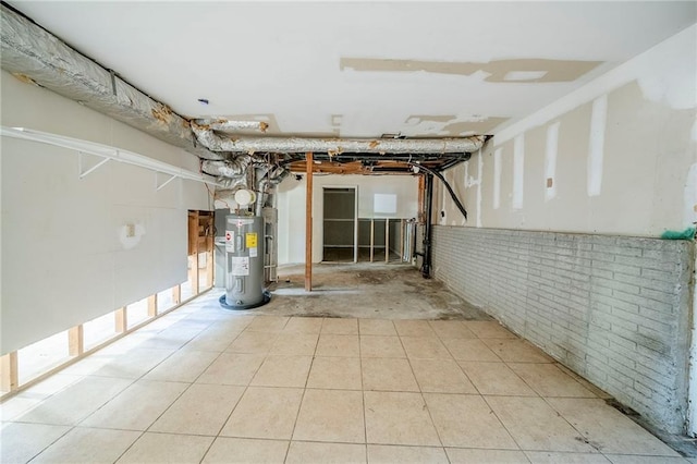 unfinished below grade area featuring brick wall, tile patterned flooring, and electric water heater