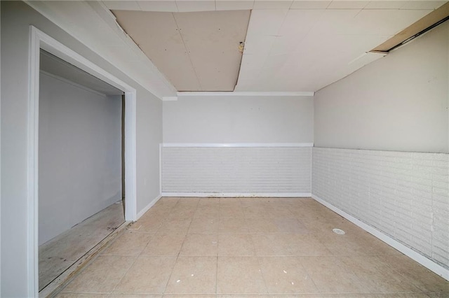 interior space with tile patterned flooring, wainscoting, and brick wall