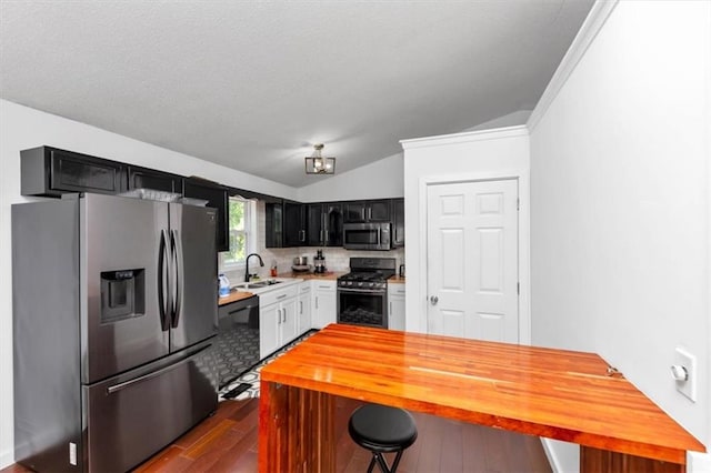 kitchen featuring appliances with stainless steel finishes, a sink, lofted ceiling, dark wood-style floors, and dark cabinetry