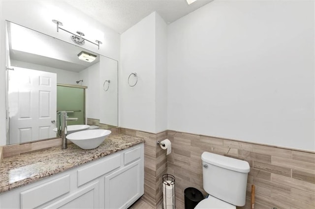 bathroom with tile walls, toilet, a wainscoted wall, vanity, and a shower